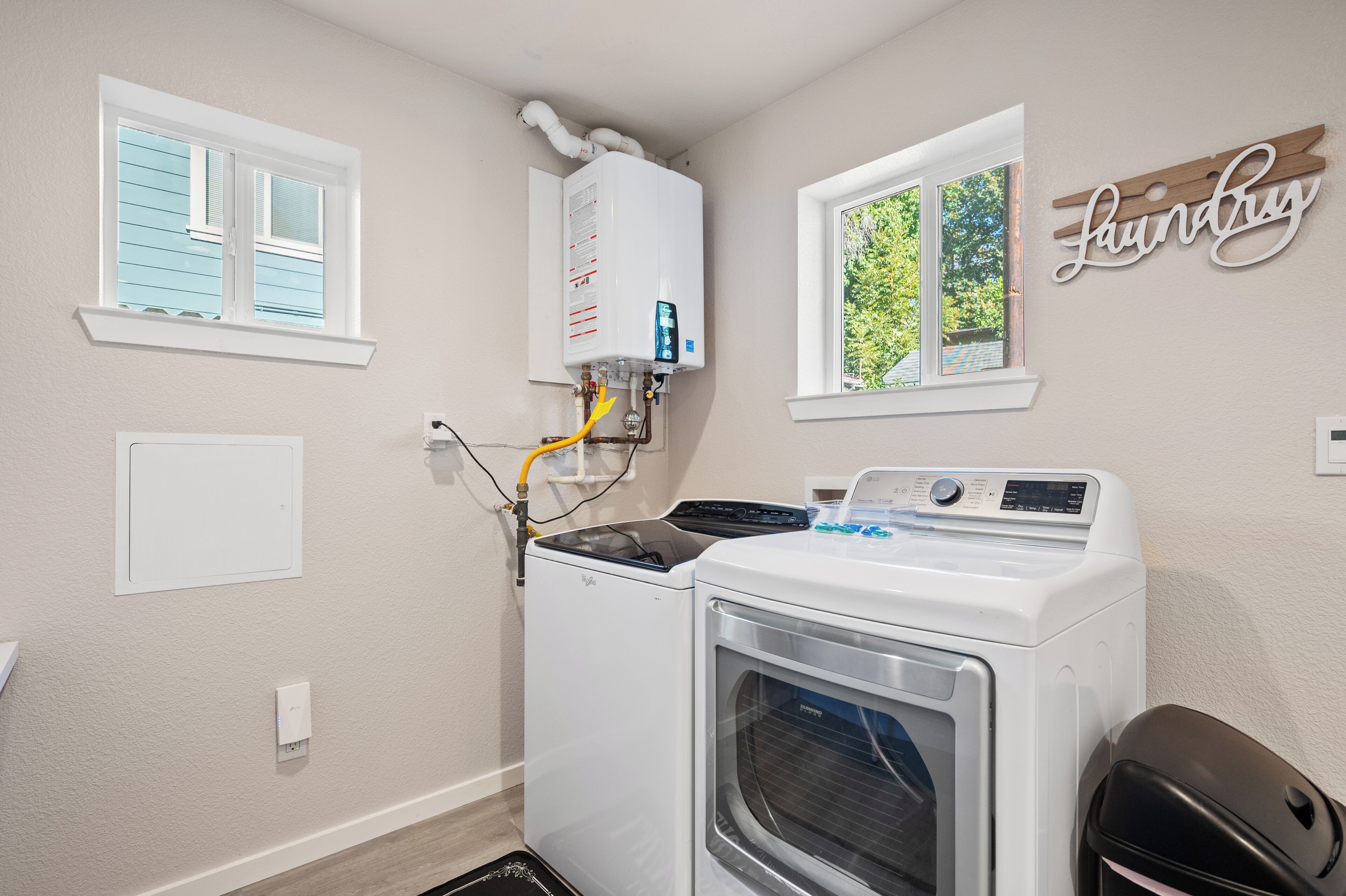 A laundry room with a washer and dryer, a water heater, and a window with a view of trees.