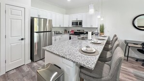 Uma cozinha moderna com armários brancos, eletrodomésticos de aço inoxidável, bancada de granito e espaço para banquetes.