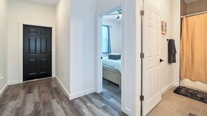 Um corredor com uma porta preta, uma porta branca que dá para um quarto e um banheiro com cortina de chuveiro.
