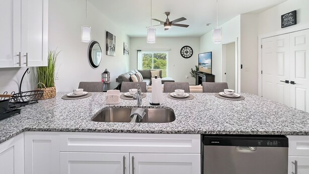 Uma cozinha moderna com bancadas de granito, armários brancos, lava-louças embutida e iluminação pendente.