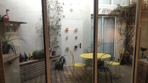 En træterrasse med et gult bord og stole, omgivet af plantekasser og en lyserød flamingo statue.