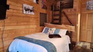 A wooden cabin room with a bed, a ladder, and a wooden door.