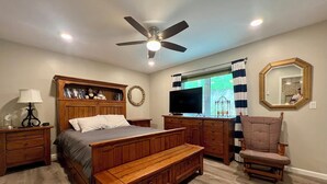 Une chambre avec un lit en bois, un banc, une télévision, un ventilateur de plafond et un grand miroir.