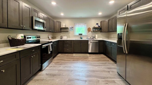 Une cuisine moderne avec des meubles de couleur sombre, des appareils électroménagers en acier inoxydable et un plancher en bois.