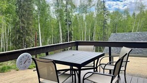 Une terrasse extérieure avec une table et des chaises, entourée d’une balustrade en bois, donnant sur une zone boisée.