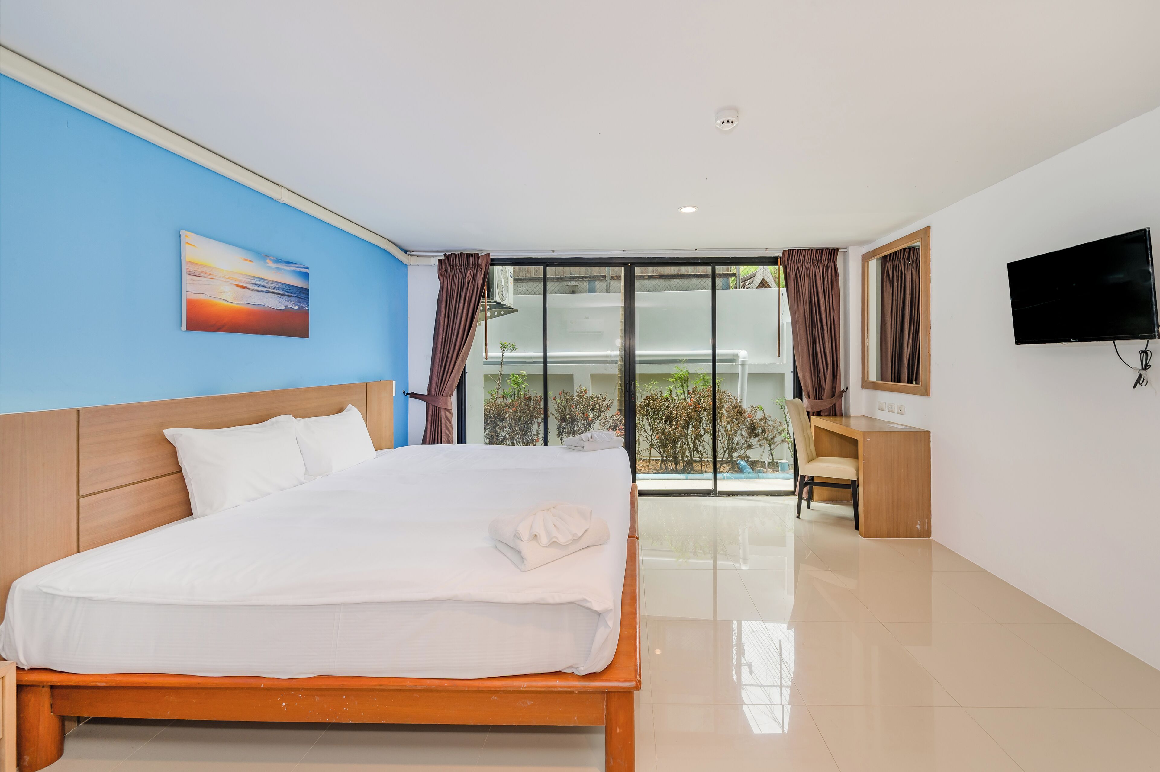 A hotel room with a bed, a desk, a TV, and a view of the outdoors.