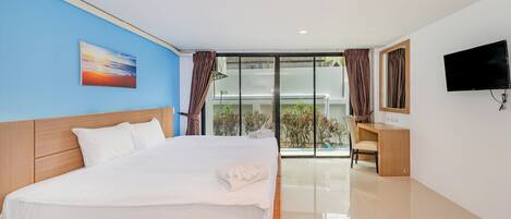 A hotel room with a bed, a desk, a TV, and a view of the outdoors.