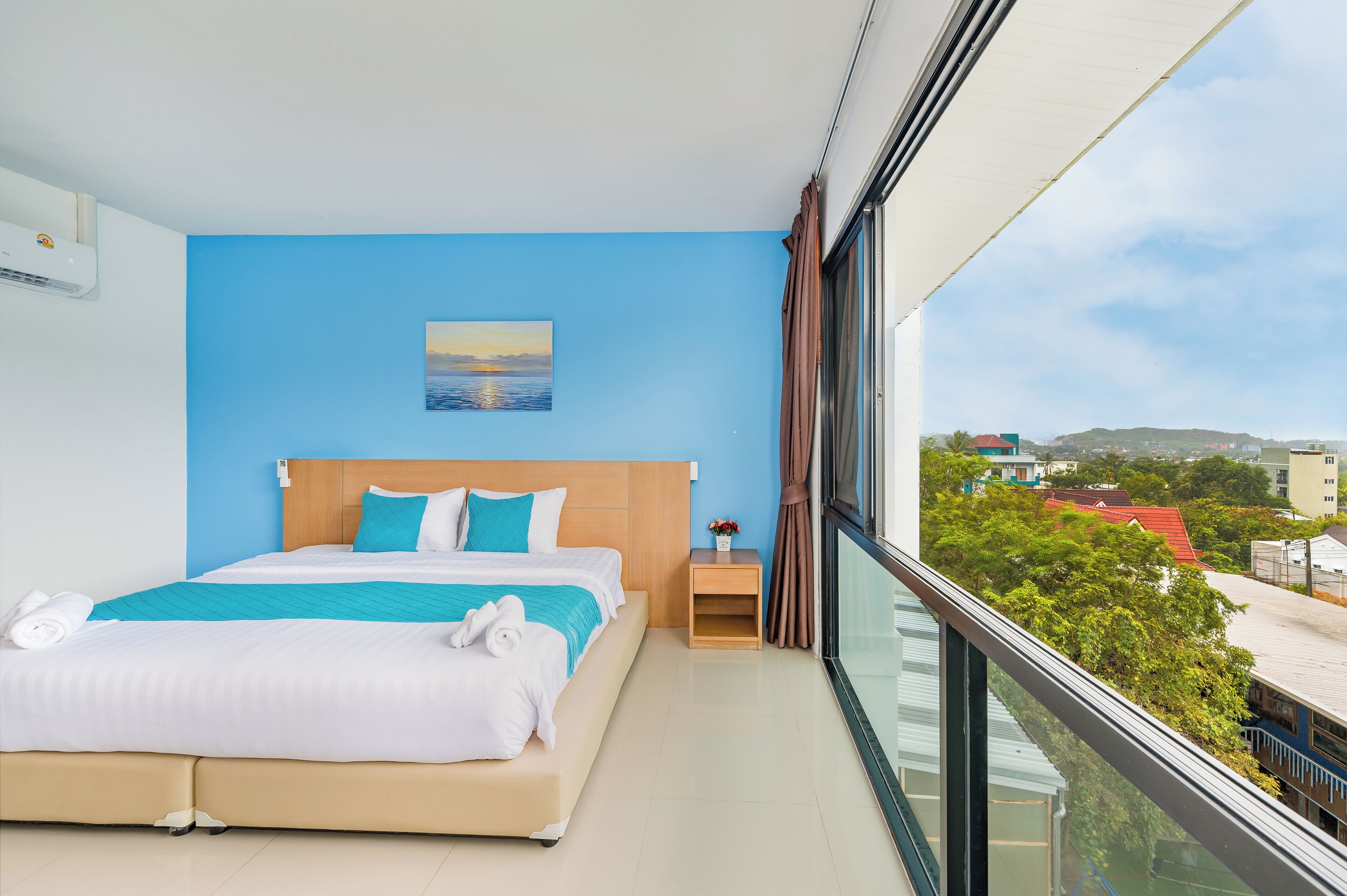 A modern hotel room with a large bed, a nightstand, a painting, and a view of the city.