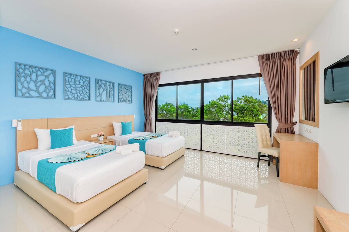 A modern hotel room with two beds, a desk, and a large window with a view of greenery.