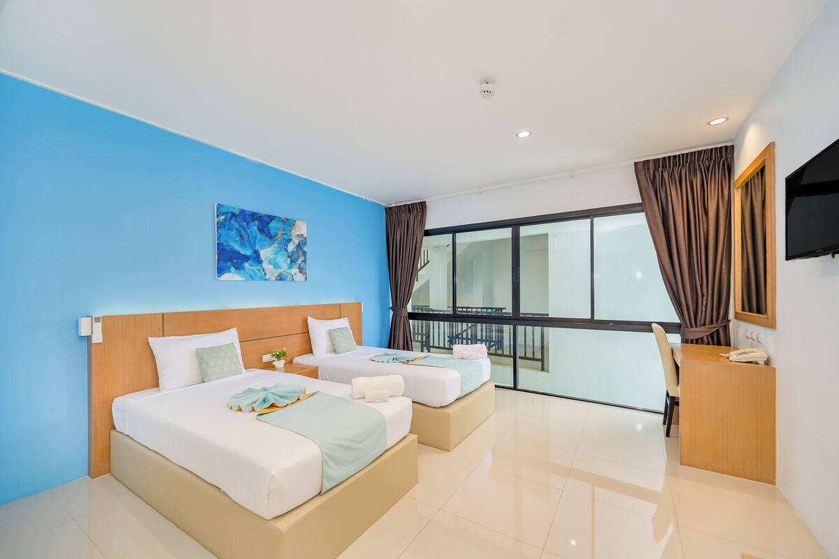 A modern hotel room with two beds, a desk, and a large window with curtains.