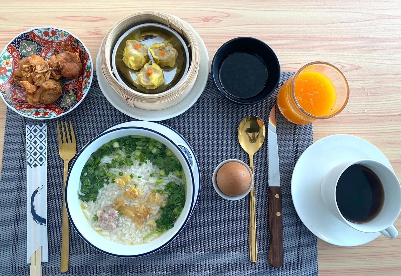 Una mesa con comida que incluye arroz, sopa, albóndigas, pollo frito y un vaso de jugo de naranja.