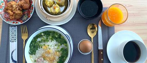 Una mesa con comida que incluye arroz, sopa, albóndigas, pollo frito y un vaso de jugo de naranja.