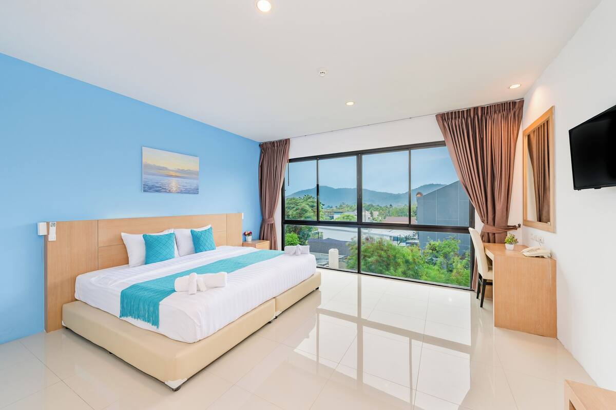 A modern hotel room with a large bed, a desk, and a view of the city.