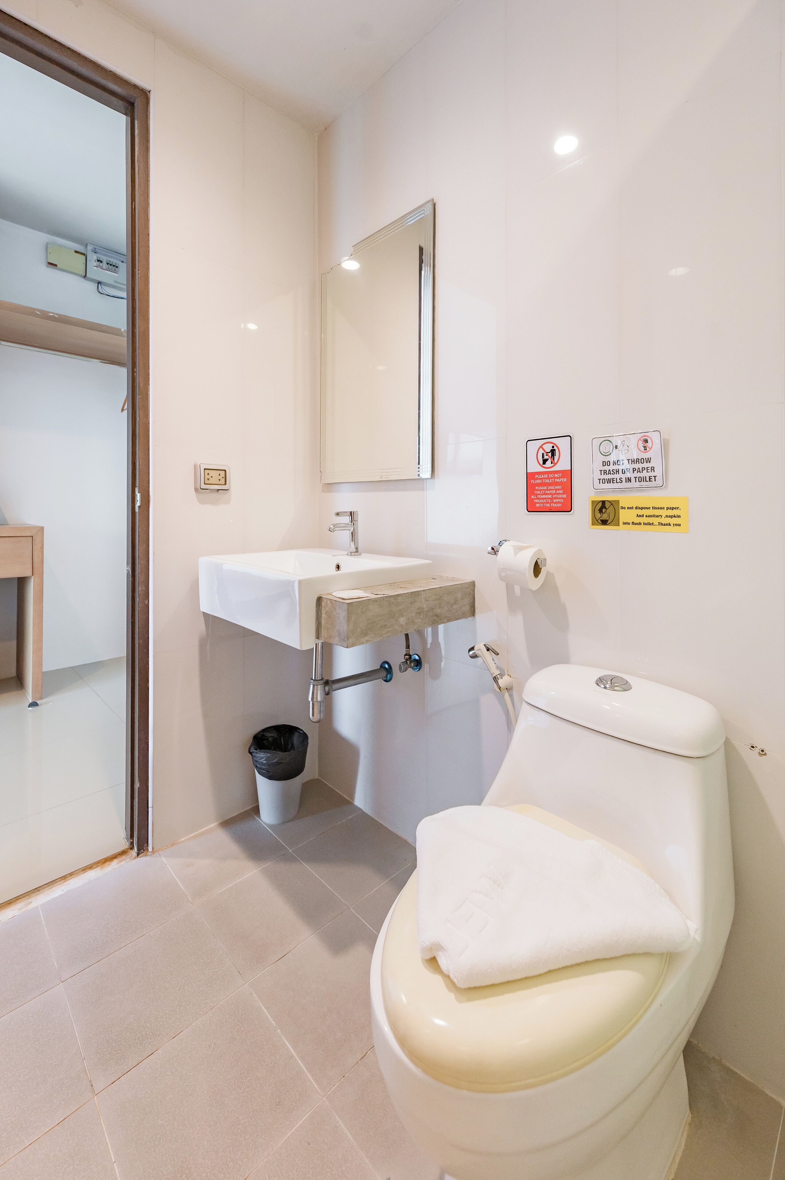 Een badkamer met toilet, wastafel en spiegel. Er hangen bordjes aan de muur en er staat een afvalbak.