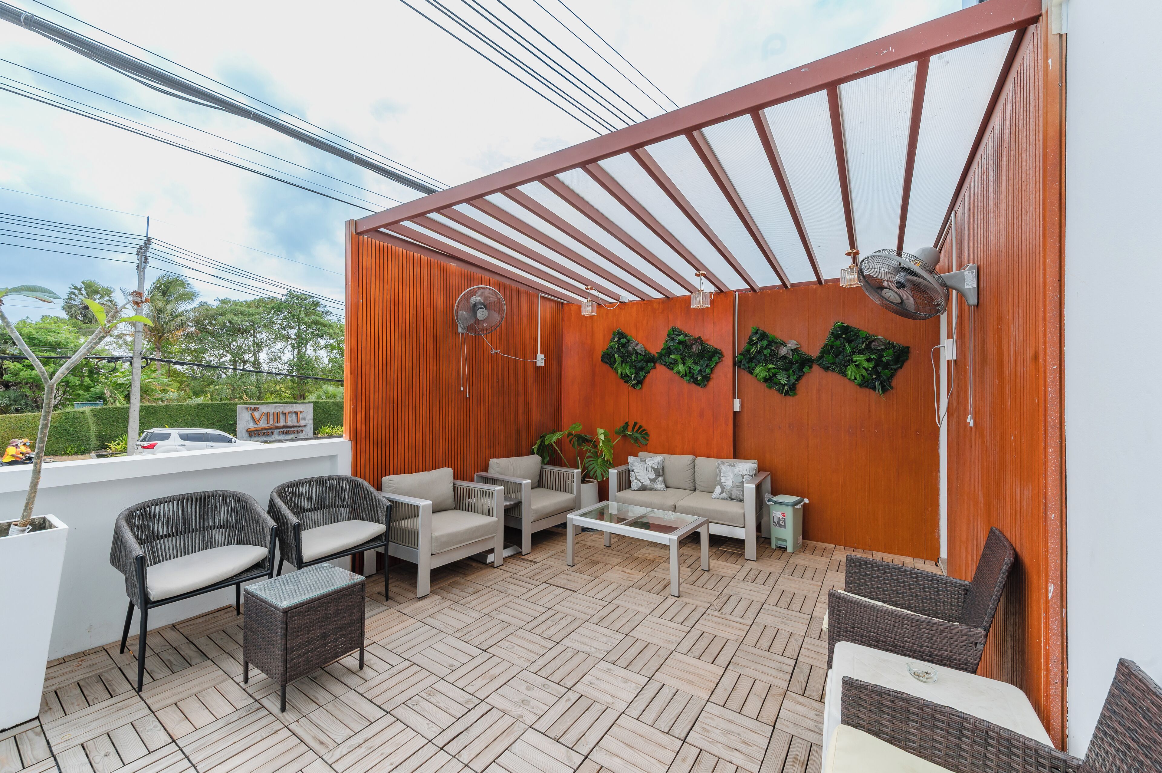 Een terras buiten met rieten meubilair, een witte tafel en een houten wand versierd met groene planten.