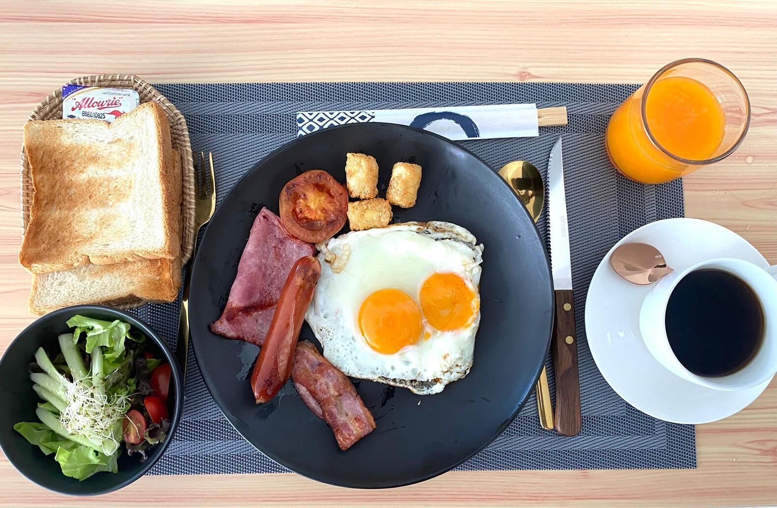 A breakfast plate with toast, bacon, eggs, and a side salad on a table with a placemat.