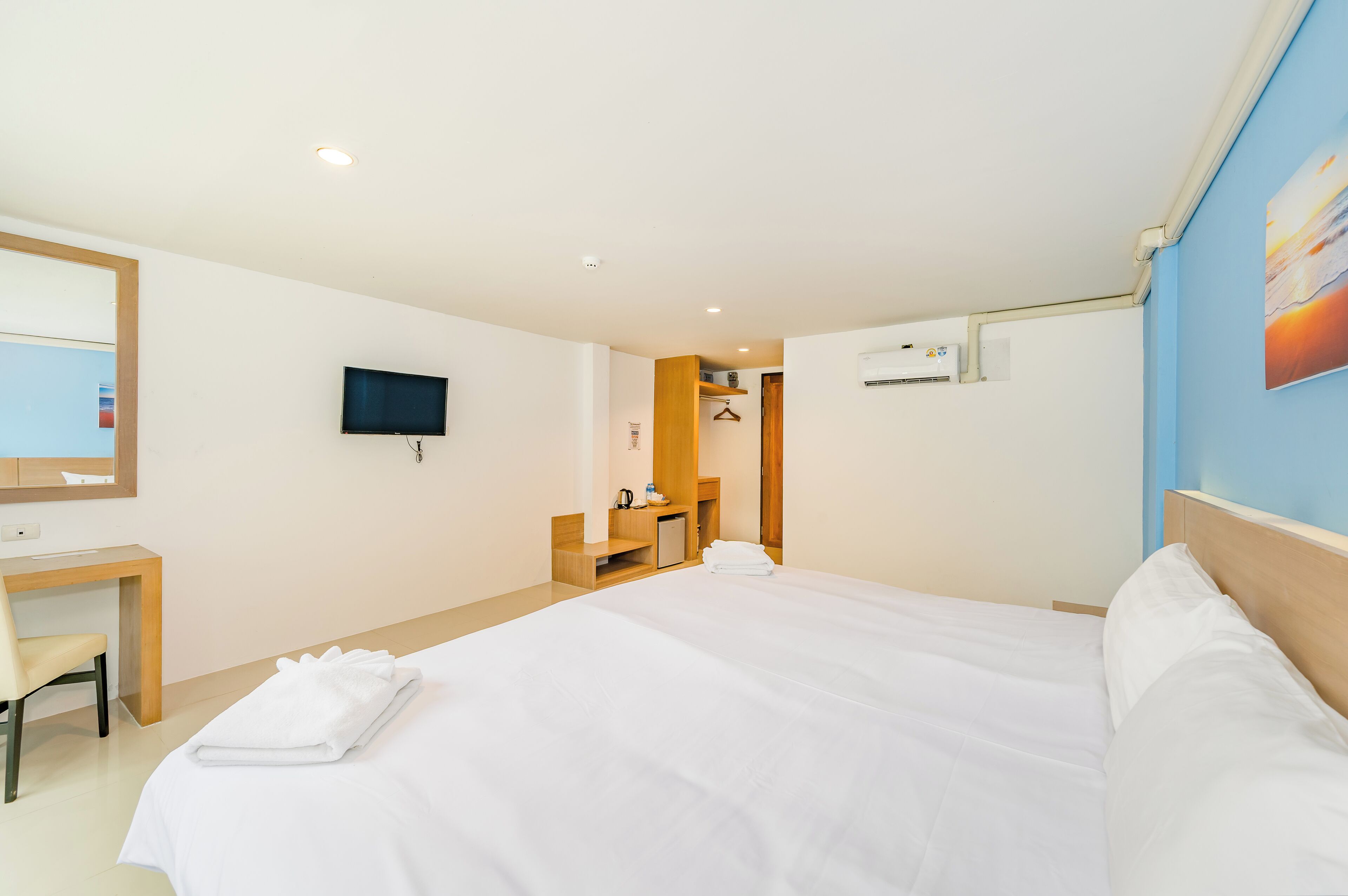 A hotel room with a bed, a desk, a chair, a television, and a bathroom visible through an open door.