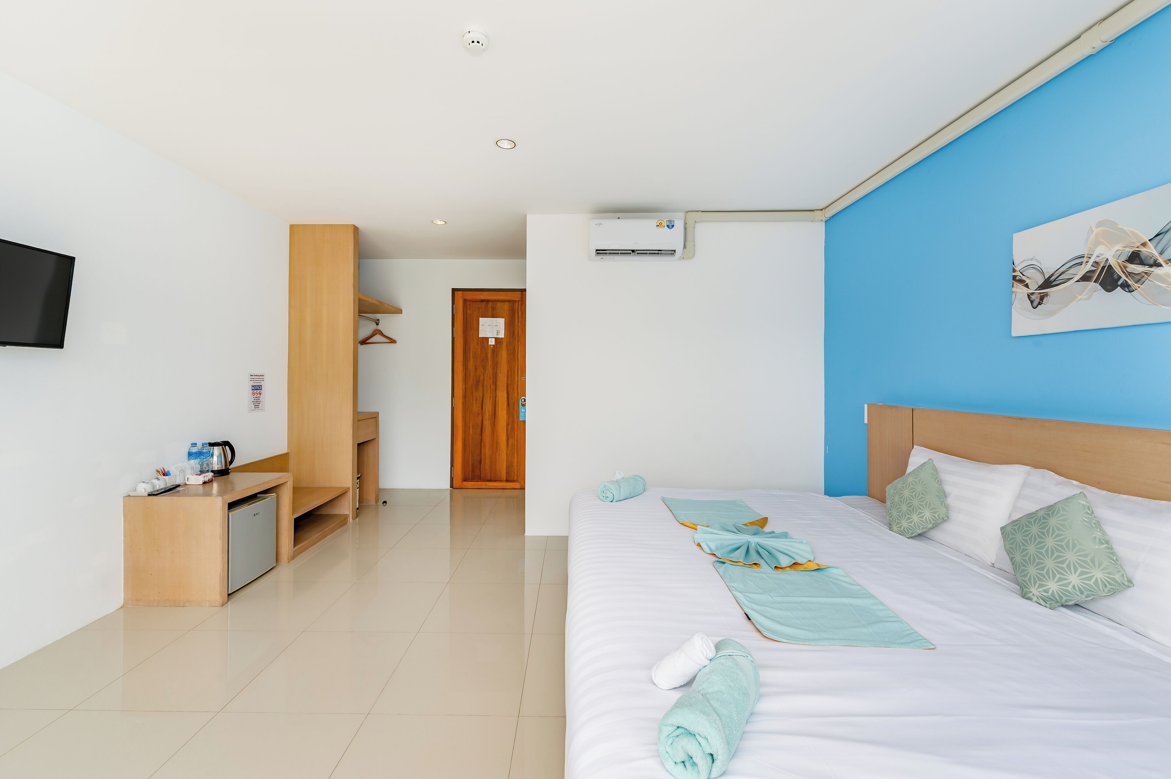 A hotel room with a bed, a desk, a small kitchenette, and a TV.