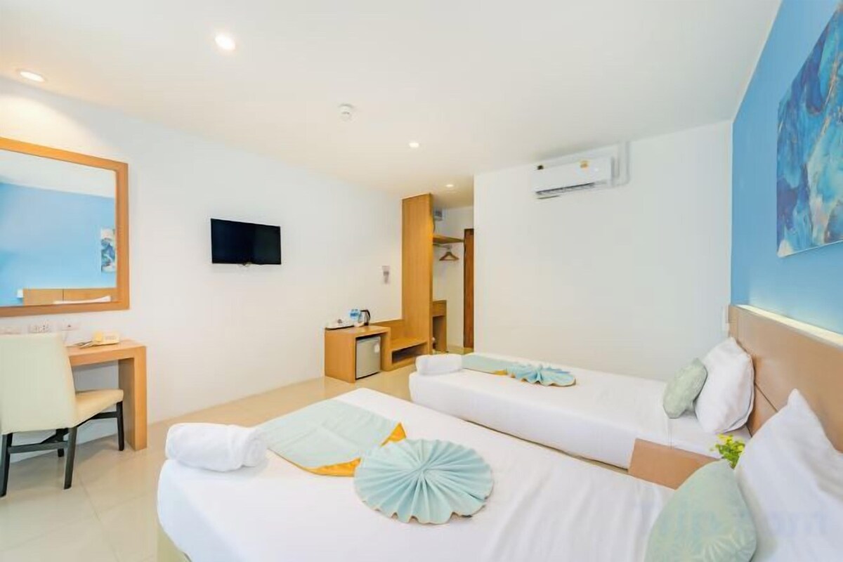 A hotel room with two beds, a desk, a chair, a television, and a bathroom visible through an open door.