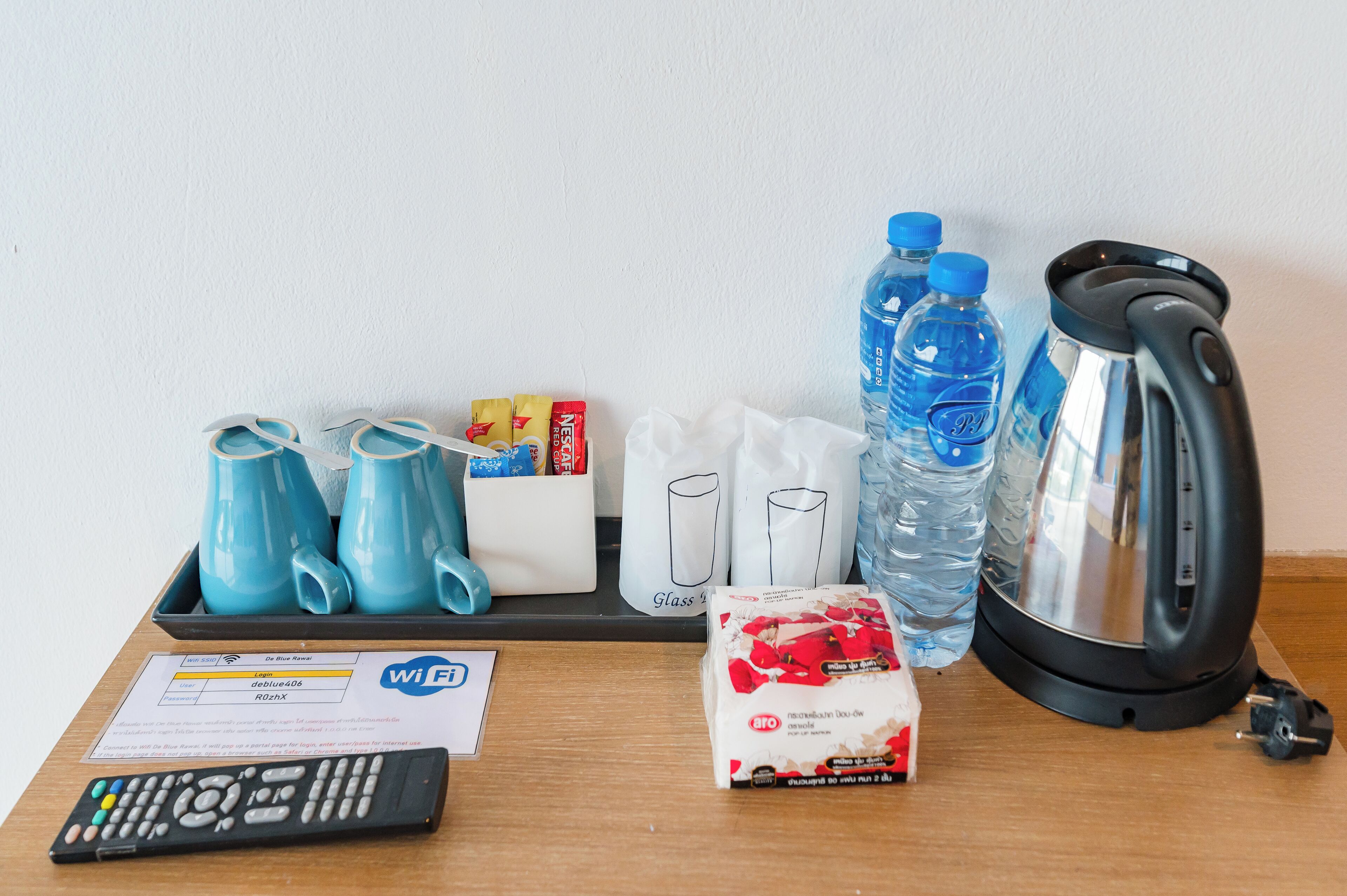 Una bandeja con un control remoto, un letrero de Wi-Fi, una caja de pañuelos, una tetera, botellas de agua y un paquete de pañuelos.