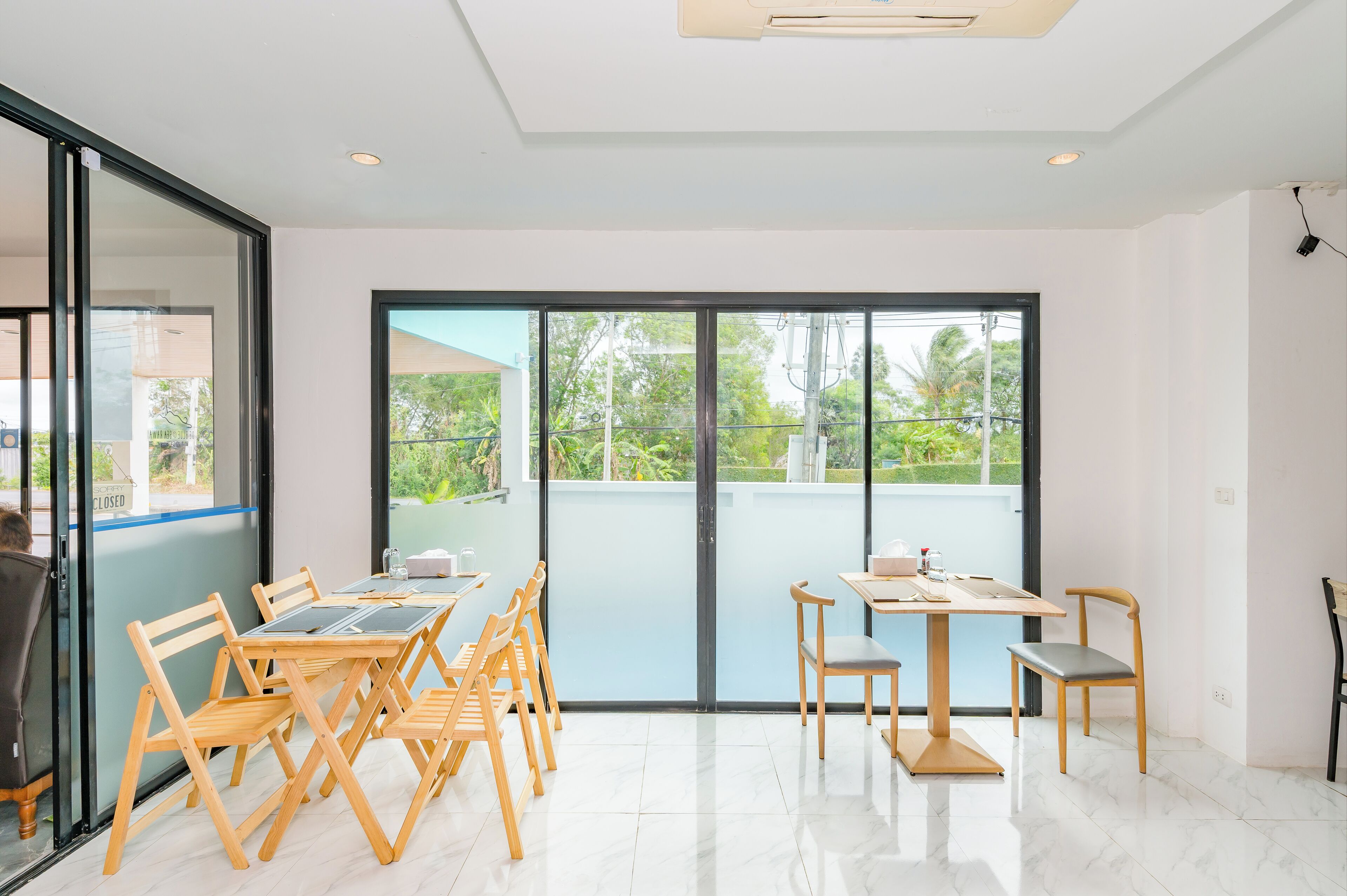 A modern room with a large sliding glass door leading to a balcony, a dining area with wooden furniture, and a clean, tiled floor.