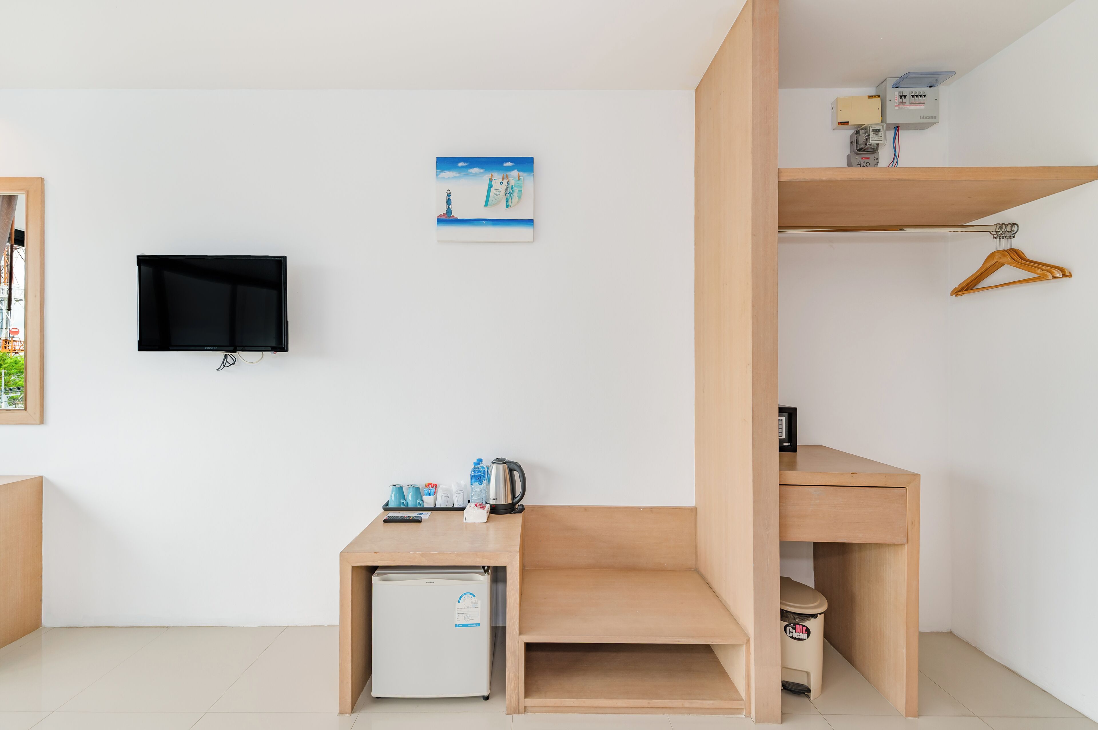 Habitación compacta con cama, escritorio, refrigerador pequeño, televisor y estante de pared con calefactor y perchero.