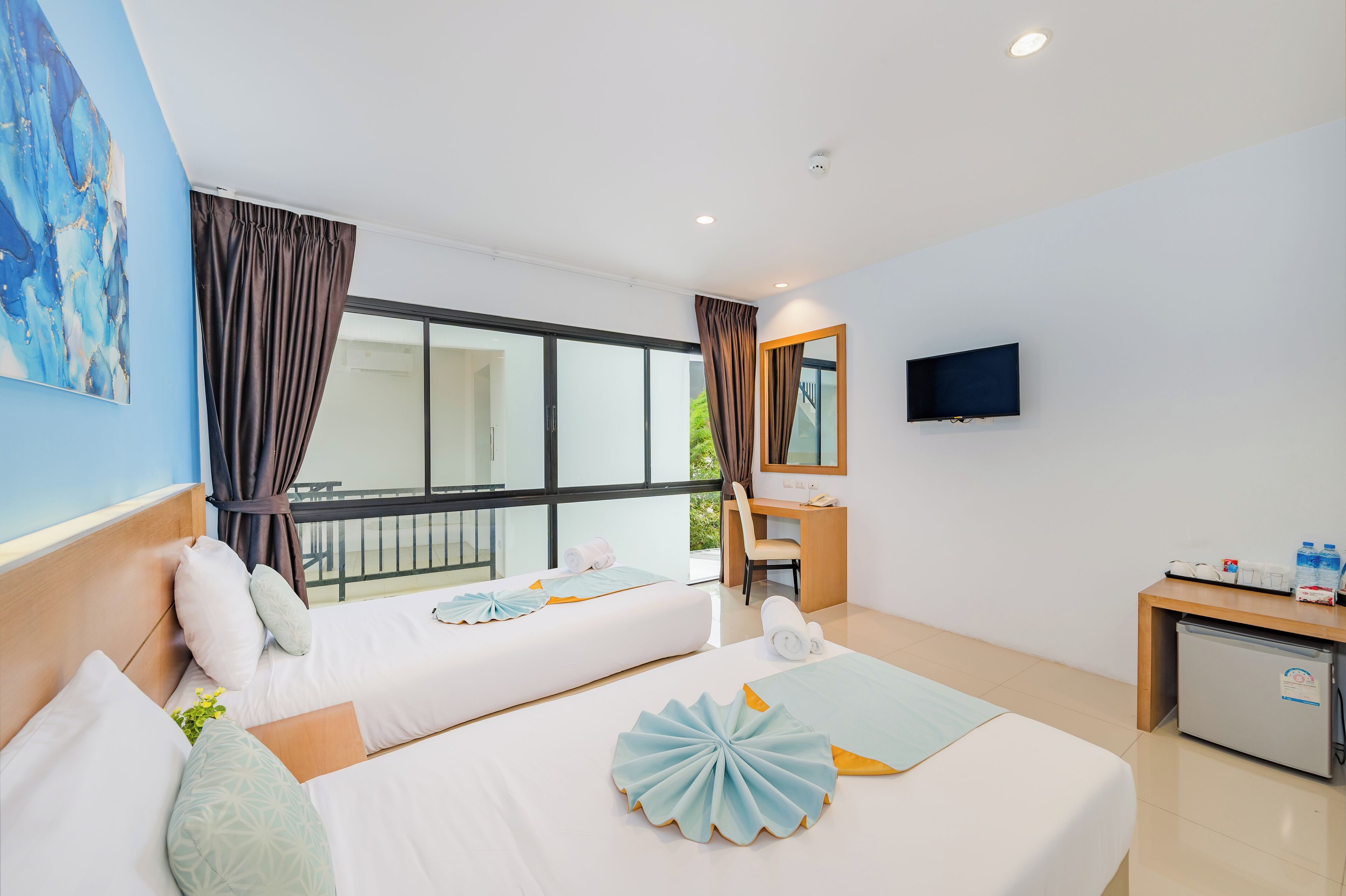 A hotel room with two beds, a desk, a chair, a television, and a small refrigerator.
