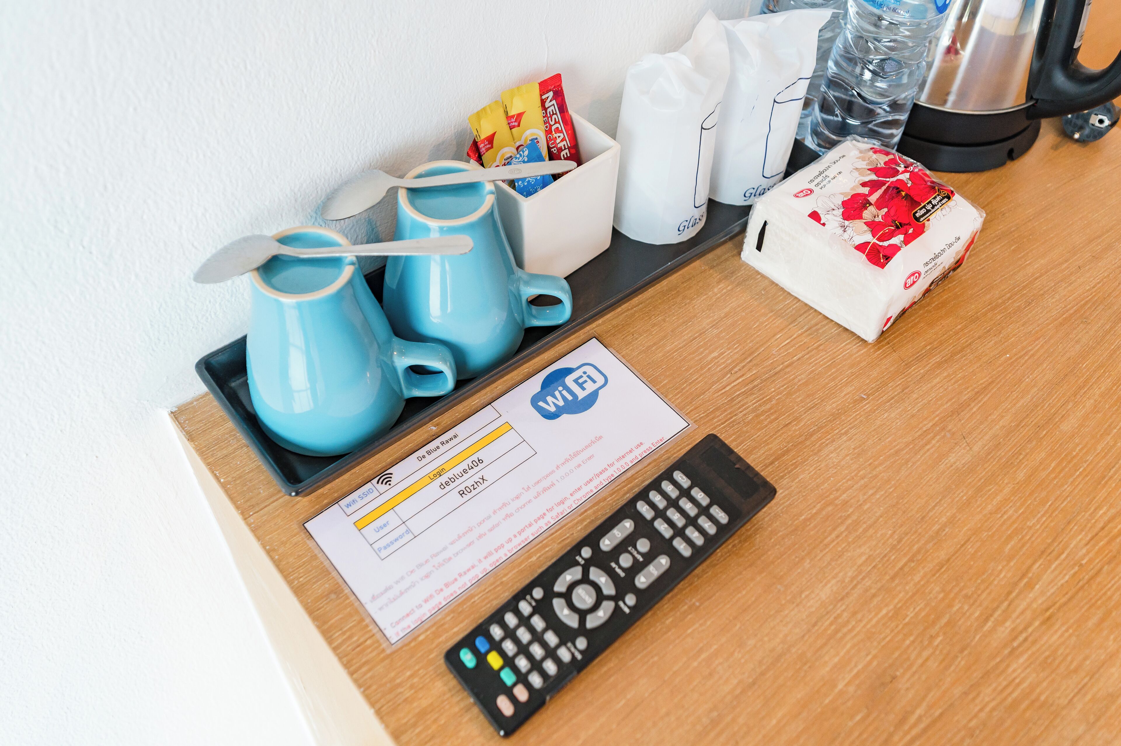 Escritorio en una habitación de hotel con un control remoto, un cartel de Wi-Fi, una cafetera y algunos artículos de aseo.