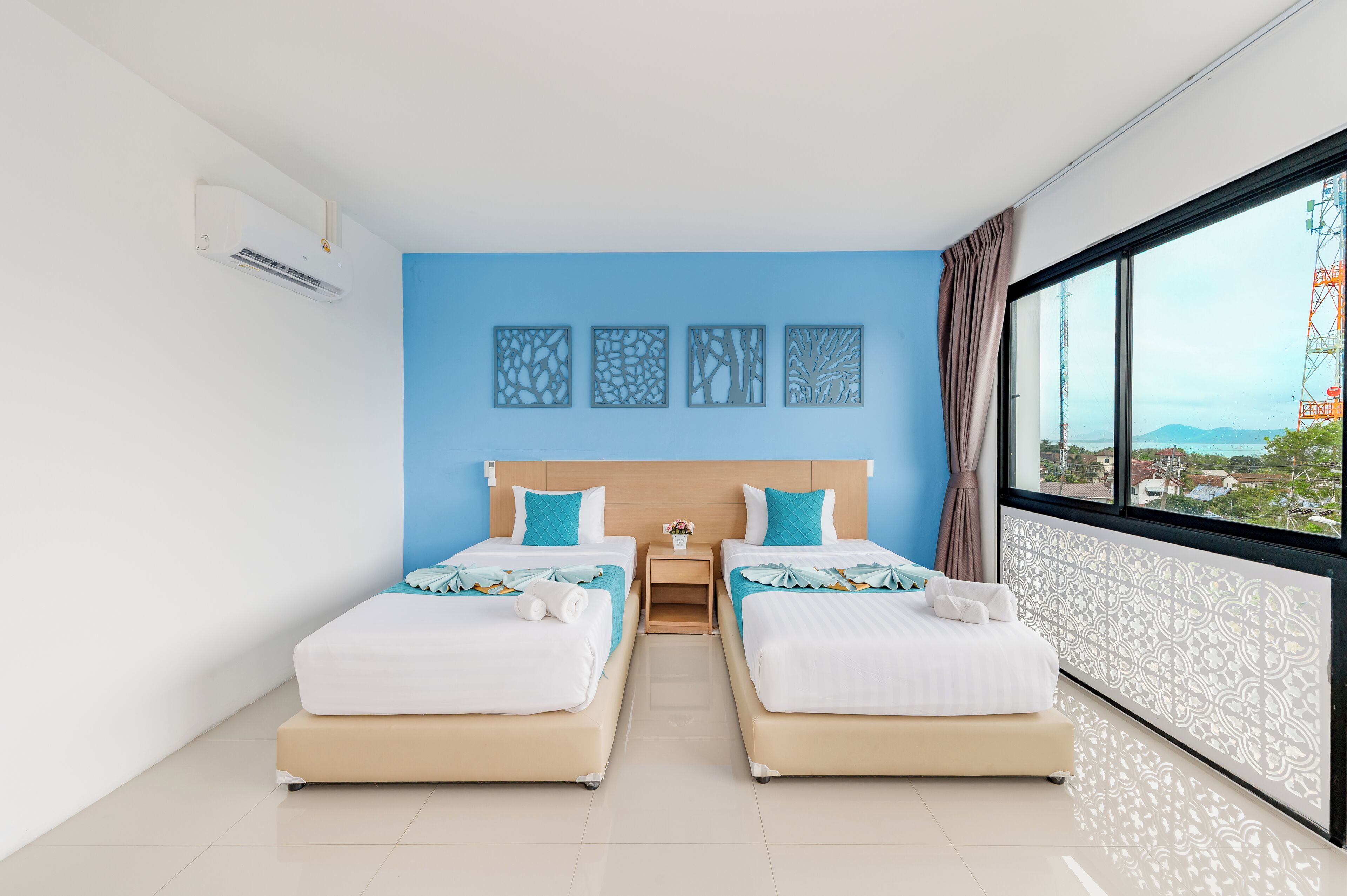 A hotel room with two beds, a large window with a view, and a wall-mounted air conditioner.