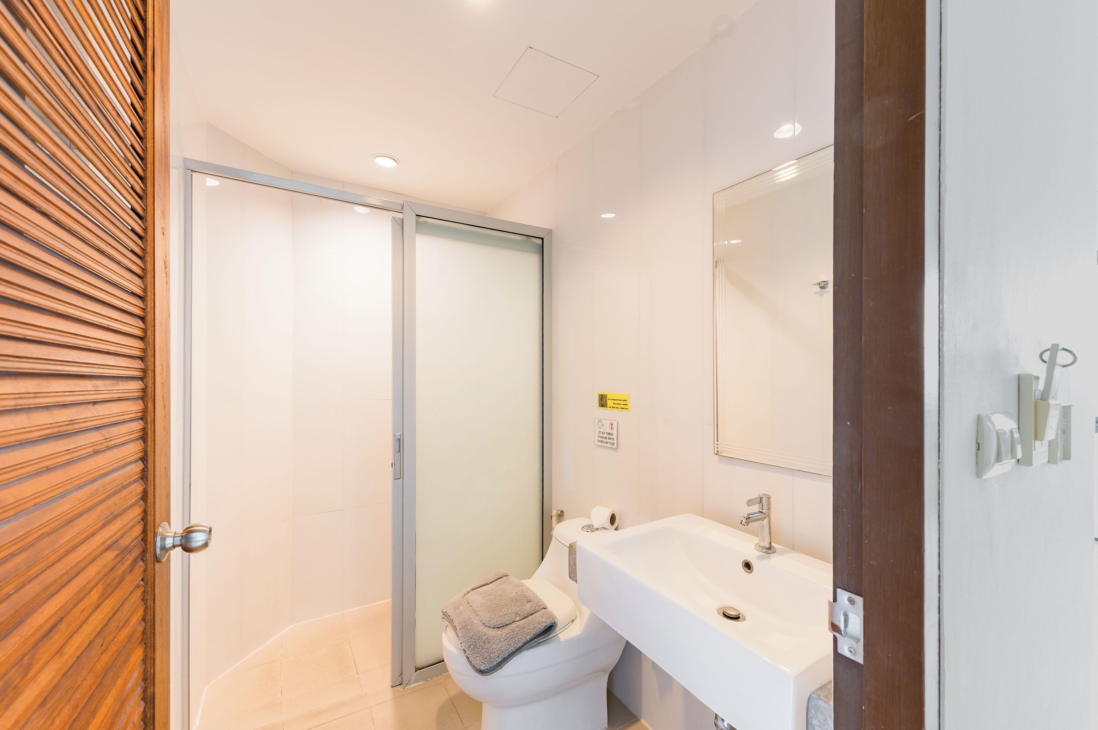 Une salle de bain moderne avec une douche à l’italienne en verre, un lavabo blanc et un grand miroir.