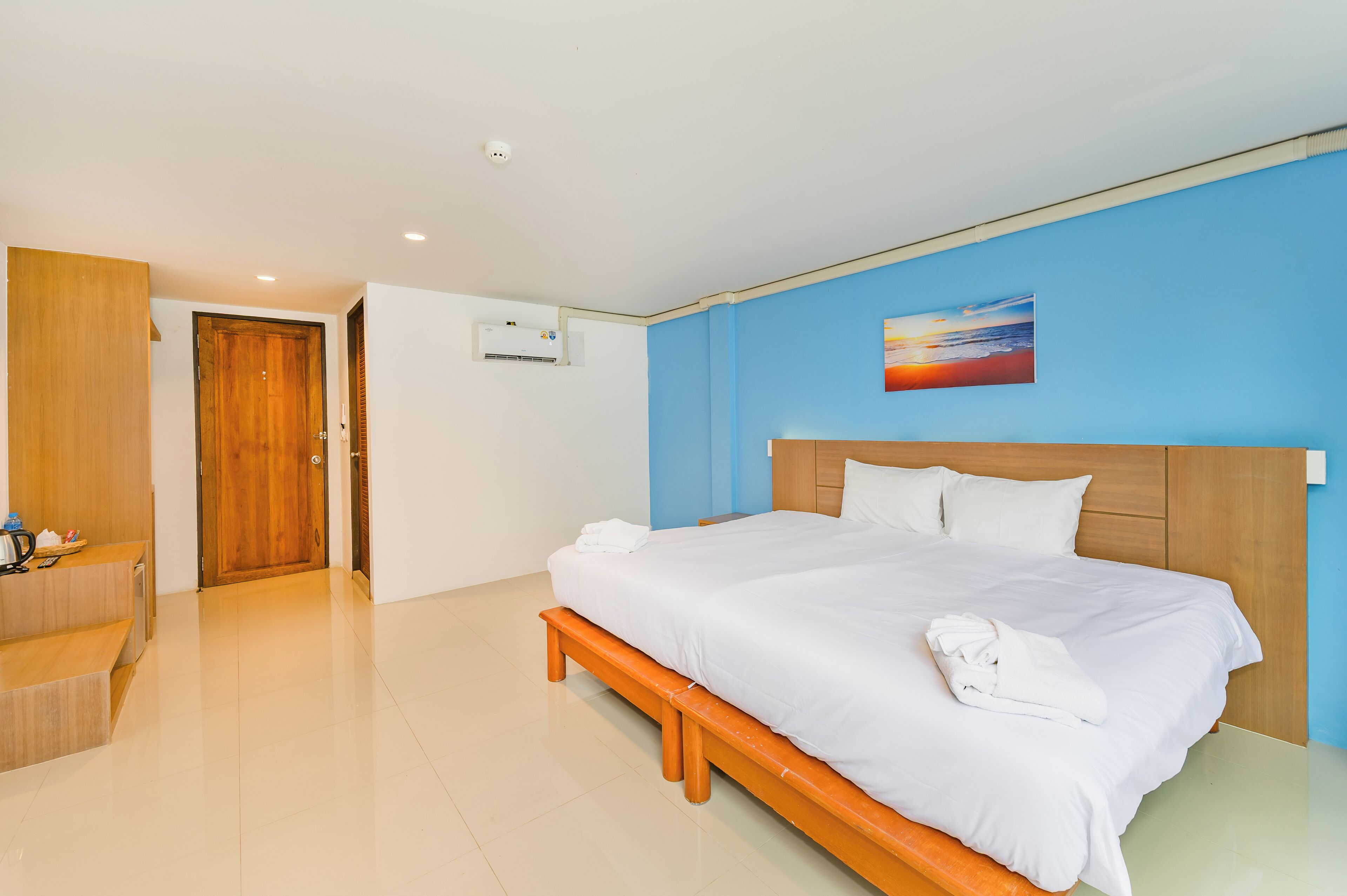 A hotel room with a large bed, a wooden bench, a desk, and a blue wall.