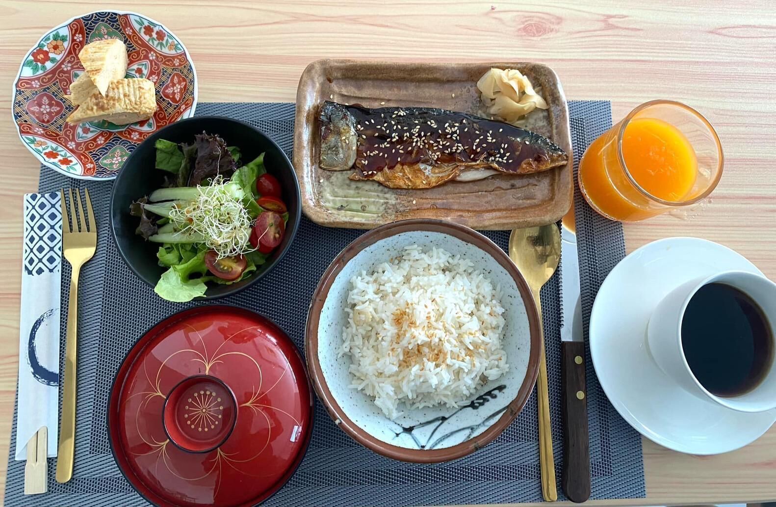 A meal with rice, fish, salad, and orange juice on a table.