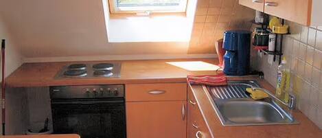 Een kleine keuken met een raam, een kookplaat, een oven, een spoelbak en essentiële voorzieningen.