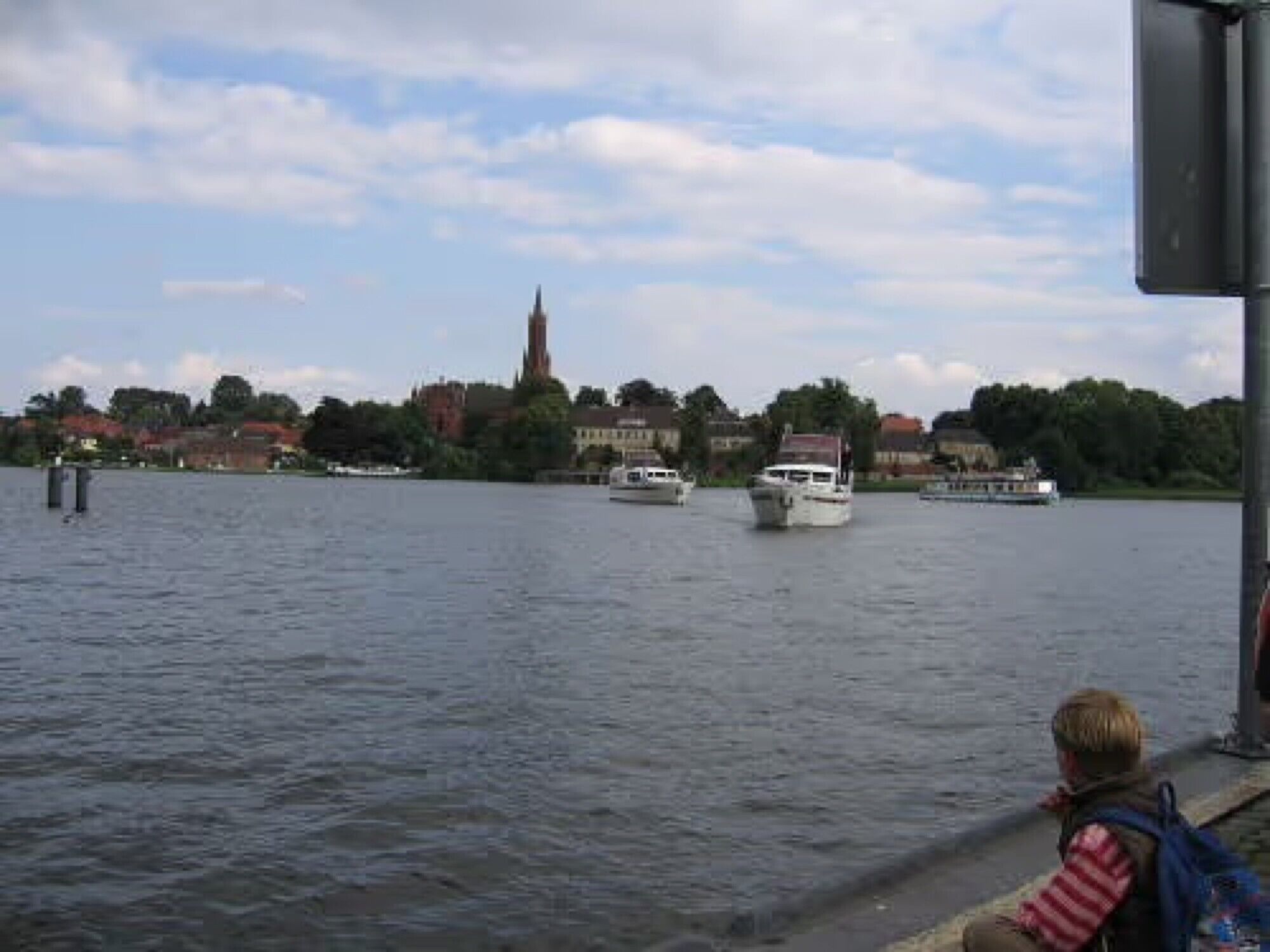 A river with boats, a distant church spire, and residential buildings.