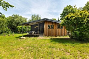 A wooden cabin with a covered porch, surrounded by a grassy yard and trees.