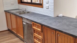 A kitchen with wooden cabinets, a stainless steel sink, and a dishwasher. - Gateway to Shoalhaven. Winter specials available now. (Bomaderry)