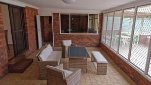 A covered patio area with wicker furniture, a glass table, and a view through a mesh screen. - Gateway to Shoalhaven. Winter specials available now. (Bomaderry)