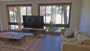A living room with a flat-screen TV on a wooden stand, a beige sofa, and a coffee table. - Gateway to Shoalhaven. Winter specials available now. (Bomaderry)