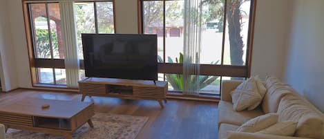 Ein Wohnzimmer mit Flachbildfernseher auf einem Holzboden, einem beigefarbenen Sofa und einem Couchtisch.