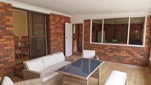 A covered patio area with a glass-top table, wicker furniture, and brick walls. - Gateway to Shoalhaven. Winter specials available now. (Bomaderry)