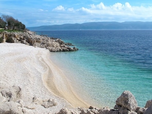 Ein Strand mit klarem türkisblauem Wasser und felsigem Gelände.