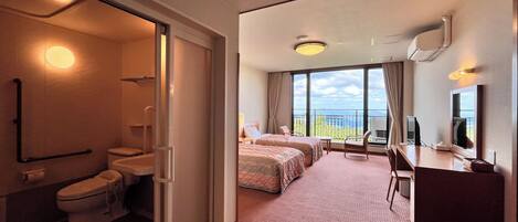 A hotel room with a bathroom, a balcony with a view, two beds, a desk, and a chair.