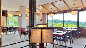 An indoor dining area with tables and chairs, a menu stand, and a view of greenery outside. - Hikosan Hotel Nagomi (Soeda)