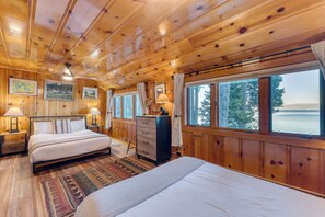 Ein Schlafzimmer in einer Holzhütte mit zwei Betten, einem Schminktisch und großen Fenstern mit Blick auf den Wald.