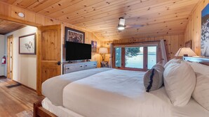 Un dormitorio con paneles de madera, una cama grande, un televisor y un ventanal con vistas al exterior.