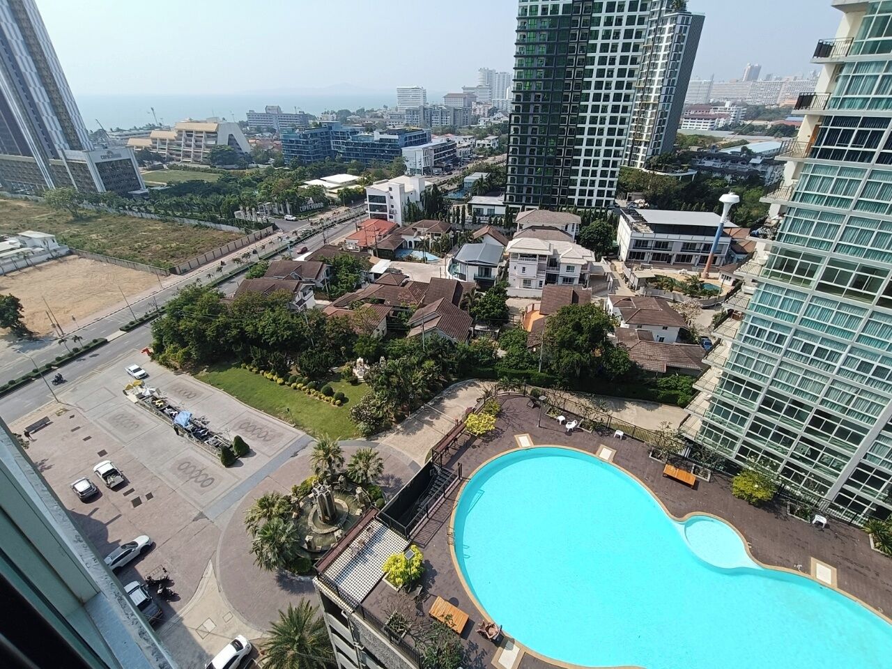 A high-rise building with a large swimming pool surrounded by greenery and residential buildings.