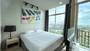 Quarto de hotel com uma cama grande, televisão, luminária e vista para a cidade pela janela.