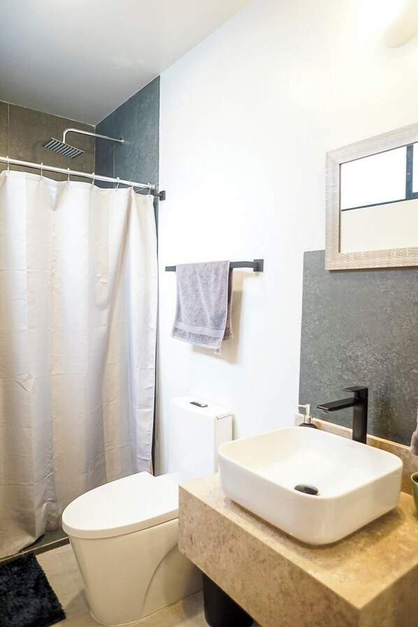 Un baño moderno con inodoro blanco, lavabo color beige y cortina de ducha.