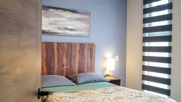 A bedroom with a bed, a nightstand, a wall-mounted painting, and a window with blinds.