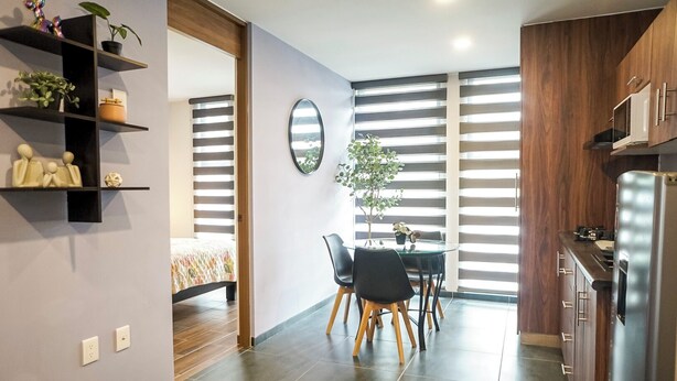 A modern kitchen with a built-in refrigerator, wooden cabinets, and a dining area with a table and chairs. - 1BR Flat with Smart Access & Parking (San Luis Potosi)